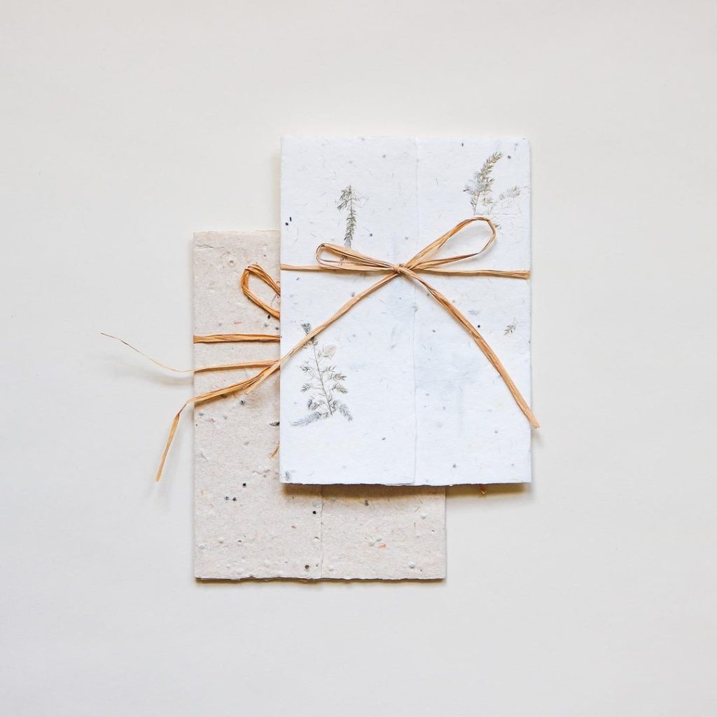Two stacks of handmade paper with pressed floral designs tied with natural twine against a plain beige background.